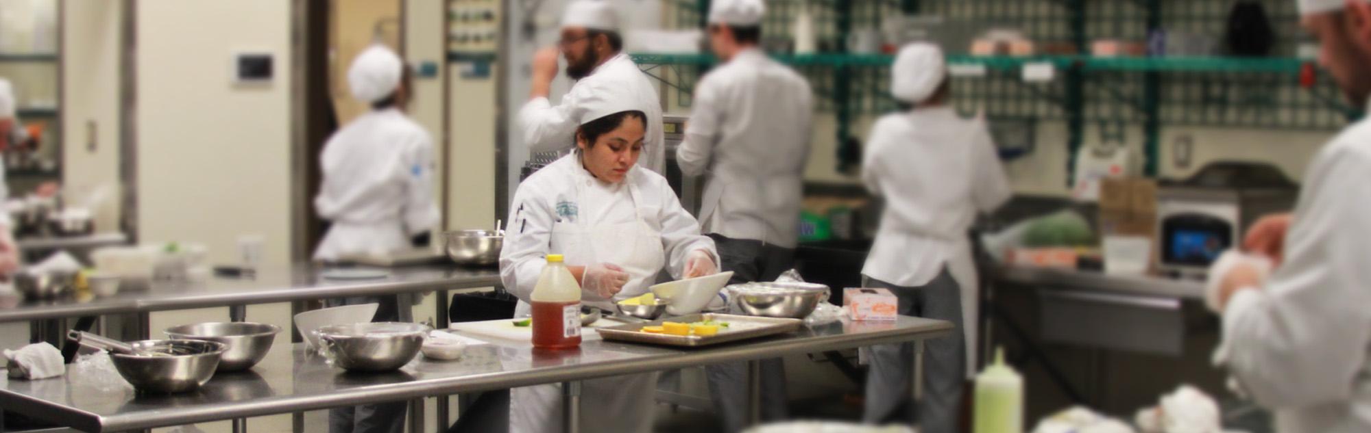 Culinary students prepare entrees in kitchen classroom.